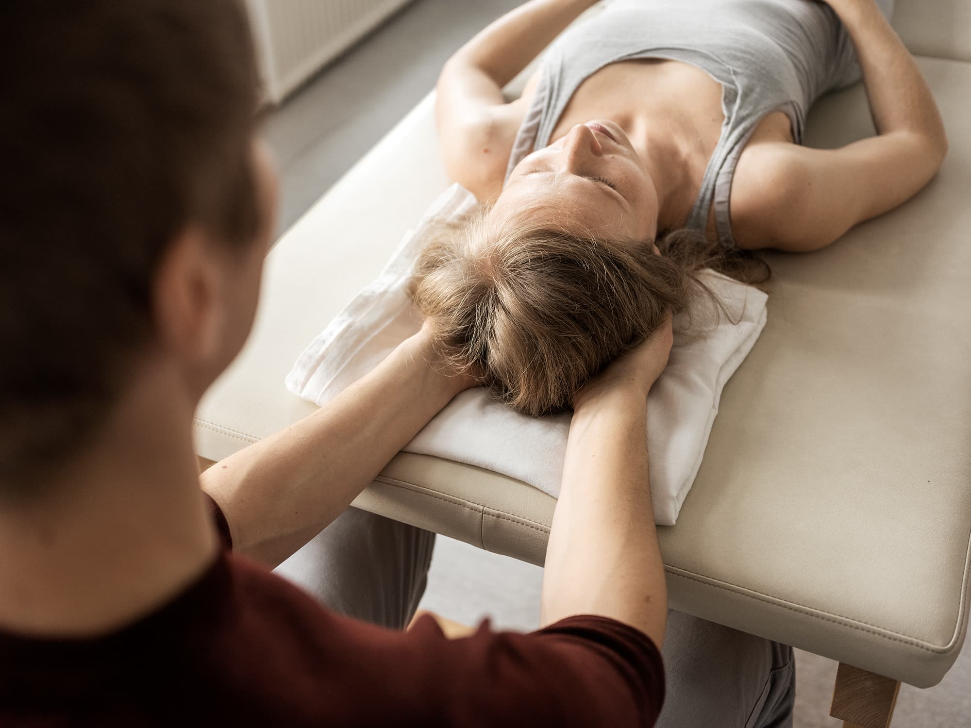 Dłonie terapeuty podtrzymują tył głowy osoby leżącej na stole do terapii